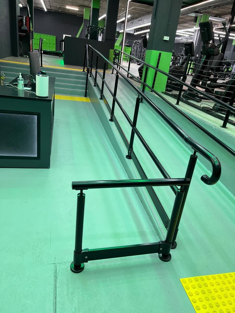 Black metal handrail along both sides of an indoor ramp in a gym